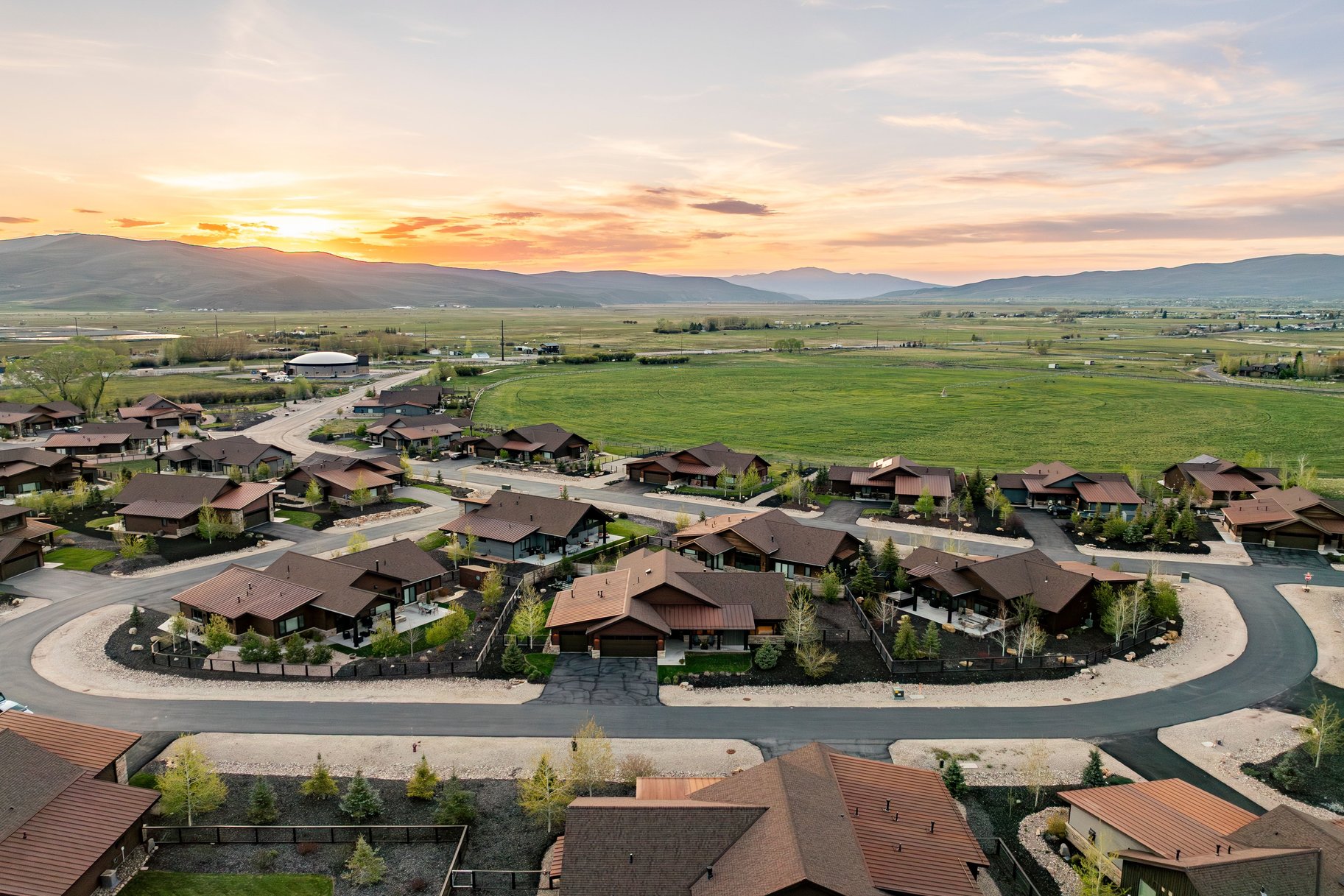 Aerial overview of a residential neighborhood with a mountain backdrop and expansive green fields