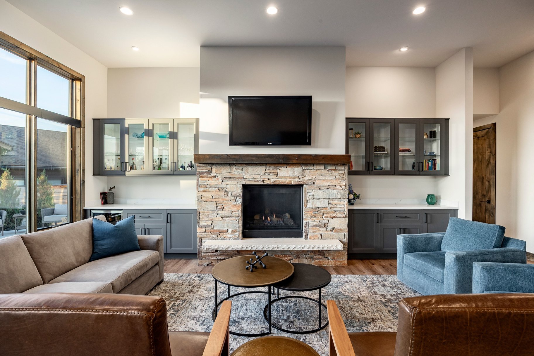 Living area featuring a stone-clad fireplace with a wood mantel, built-in cabinetry with glass-front uppers, a large window, and recessed ceiling lights