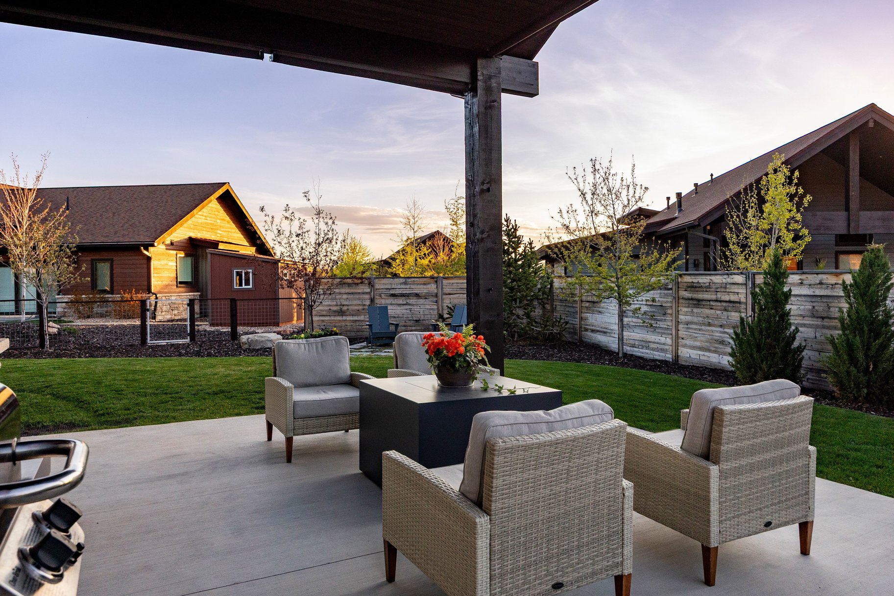 Expansive concrete patio under a dark-stained wood pergola, featuring a manicured lawn, established landscaping, and a horizontal wood fence