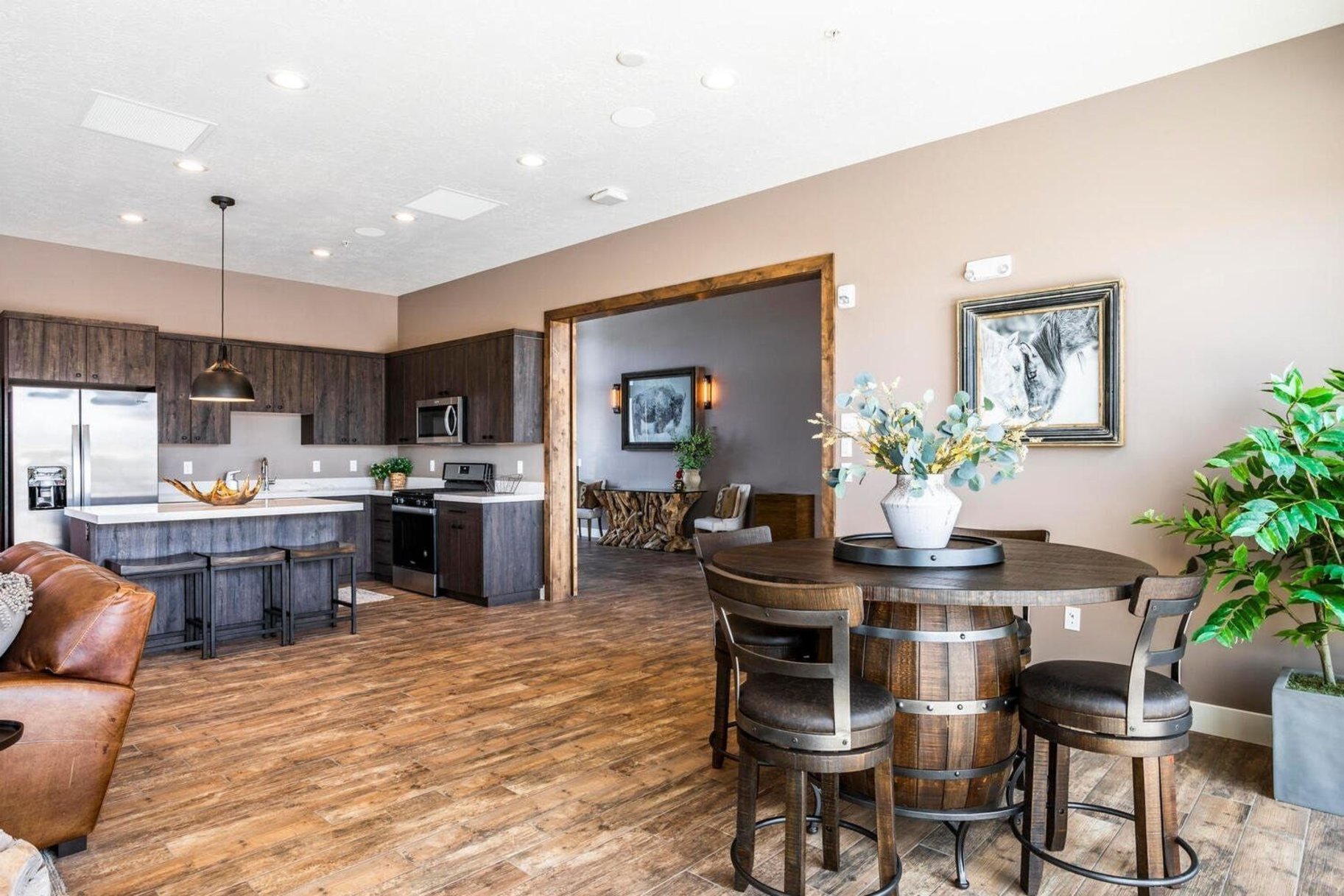 Open-concept interior featuring wood-finish flooring, a kitchen with dark cabinetry and stainless steel appliances, a kitchen island with seating, recessed lighting, and a wide entryway with wood trim