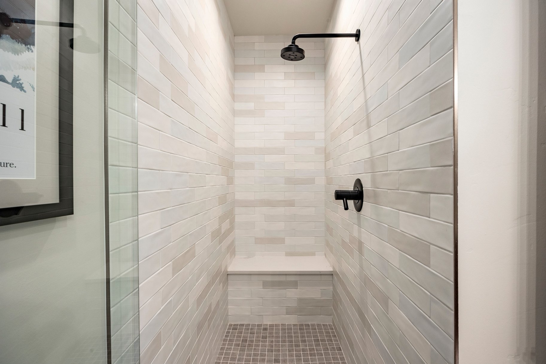Walk-in shower featuring light-toned rectangular wall tiles, a built-in bench, and matte black fixtures