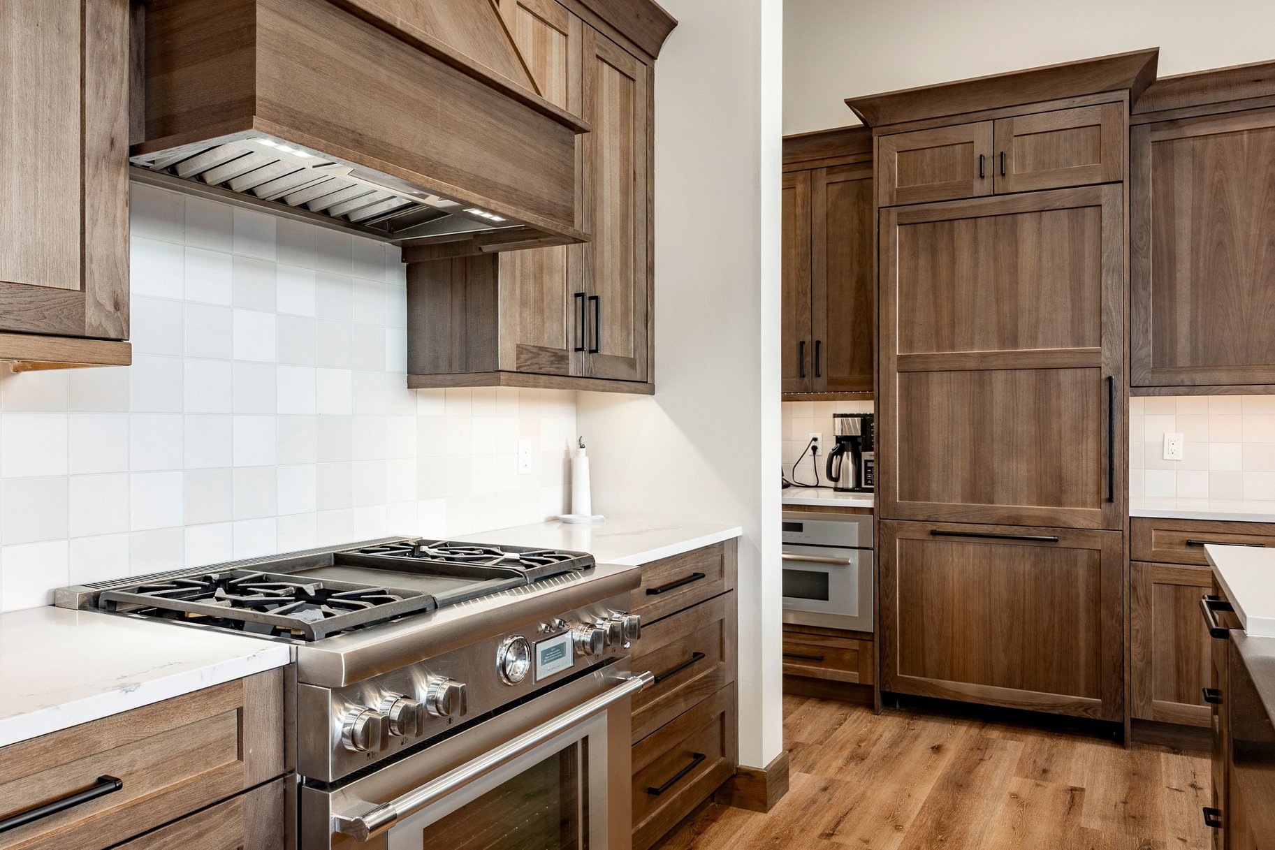 Gourmet kitchen featuring custom wood-finish cabinetry, stainless steel range with griddle, panel-ready refrigerator, white square tile backsplash, and light countertops