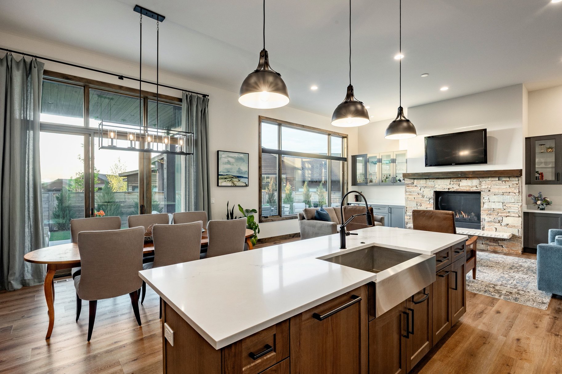 Open-concept living space featuring wood-finish flooring, a stone fireplace with a wood mantle, and an expansive kitchen island with a farmhouse sink