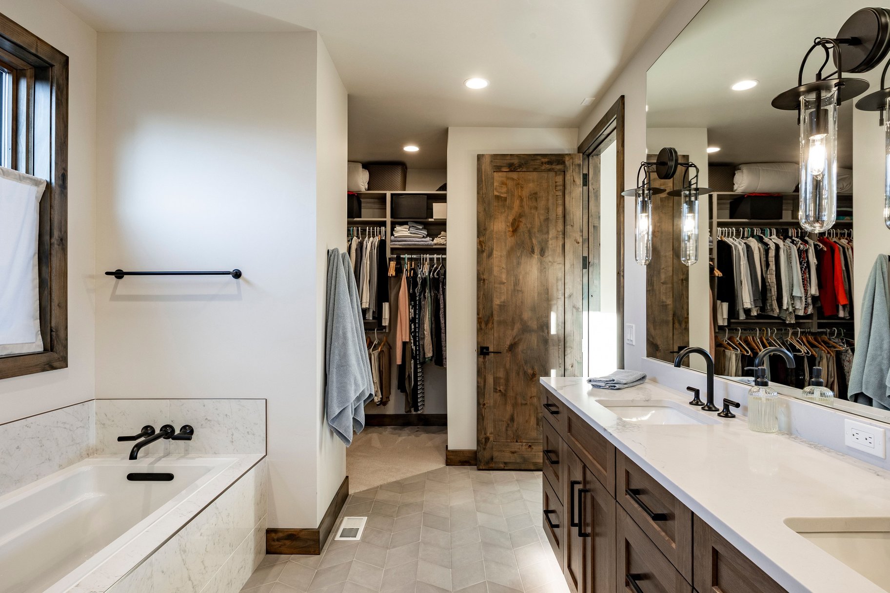 Bathroom featuring a double vanity with stone countertops, a built-in tub with matte black fixtures, an expansive walk-in closet, and wood-finish flooring