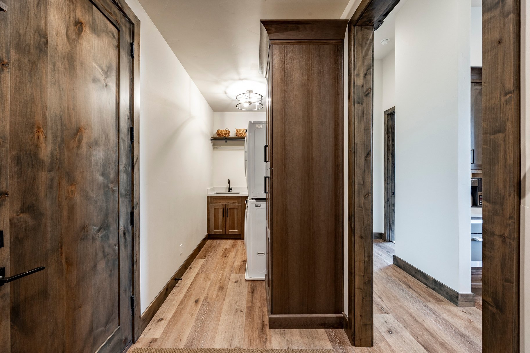 Laundry area featuring wood-finish flooring, a stacked washer and dryer, dark wood cabinetry with a sink, a wall-mounted shelf, and a ceiling-mounted light fixture