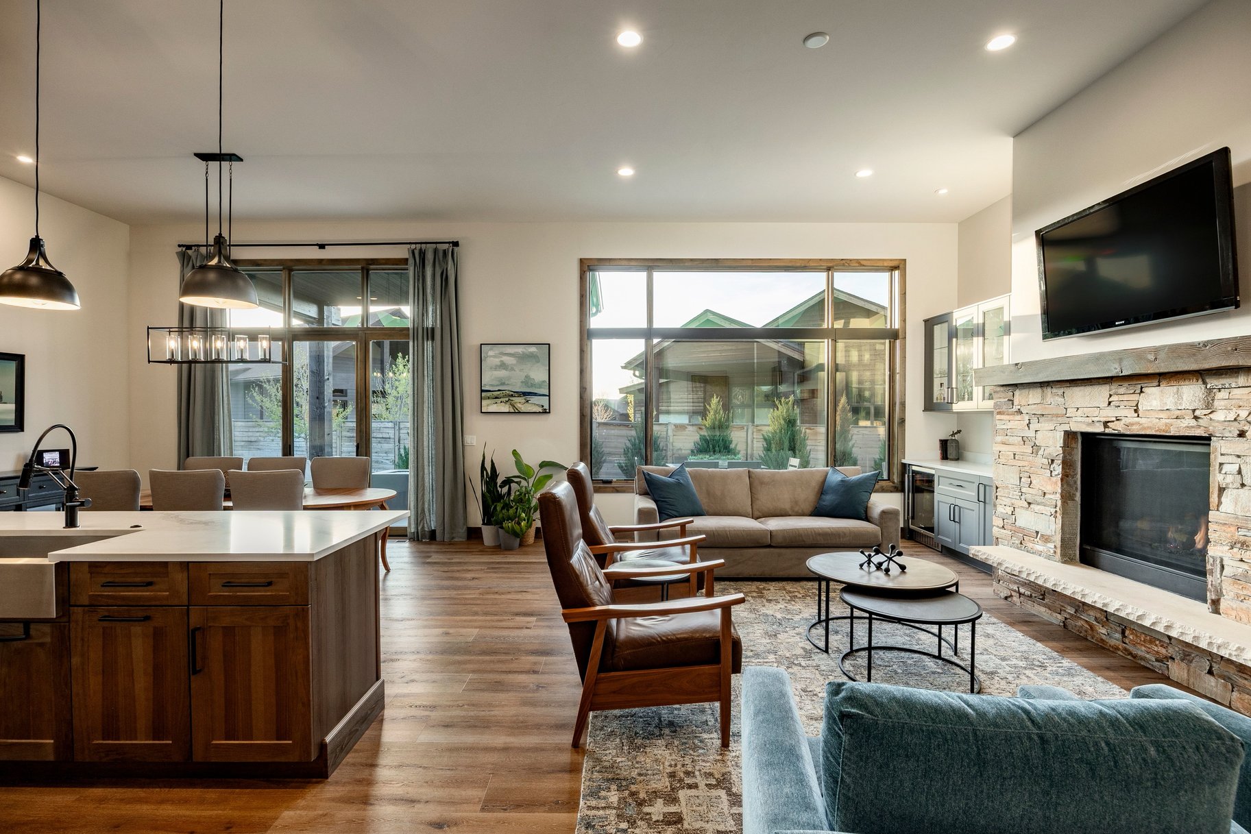 Open-concept living space featuring wood-finish flooring, a stone-clad fireplace with a hearth, and large windows