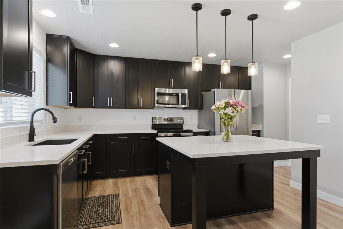 Modern kitchen featuring dark wood-finish cabinetry, white countertops, stainless steel appliances, and wood-finish flooring