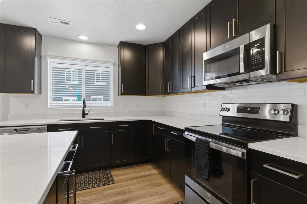 Modern kitchen featuring dark cabinetry, light countertops, stainless steel appliances, a white subway tile backsplash, and wood-finish flooring