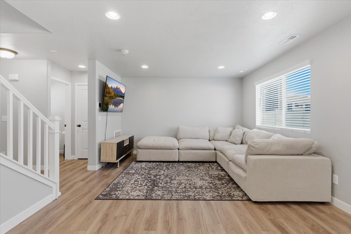 Open concept living area featuring wood-finish flooring, recessed lighting, and a large window with blinds