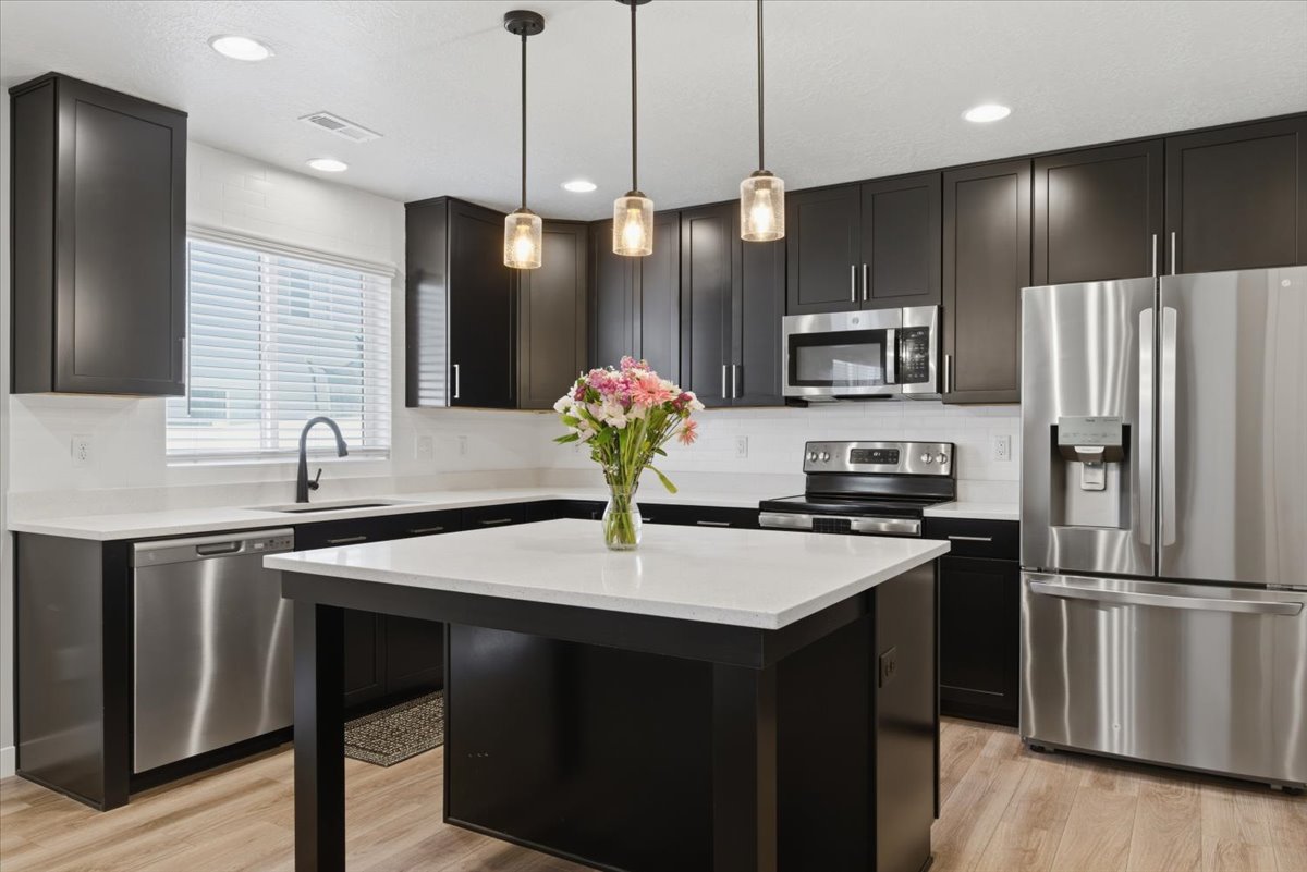 Kitchen featuring dark cabinetry, stainless steel appliances, a center island with a light-toned countertop, recessed lighting, and wood-finish flooring