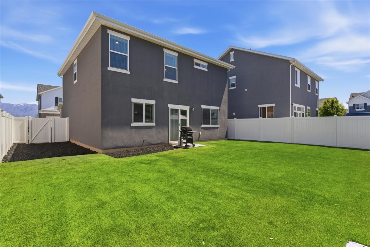 Rear exterior featuring a sliding glass door, white-framed windows, and a level lawn