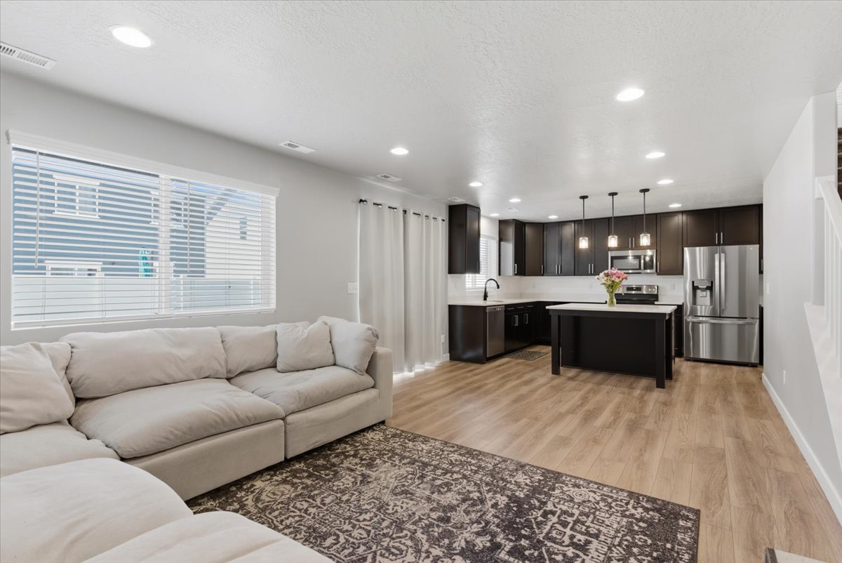 Open-concept living space featuring wood-finish flooring, recessed lighting, and a kitchen with dark cabinetry, light countertops, and stainless steel appliances