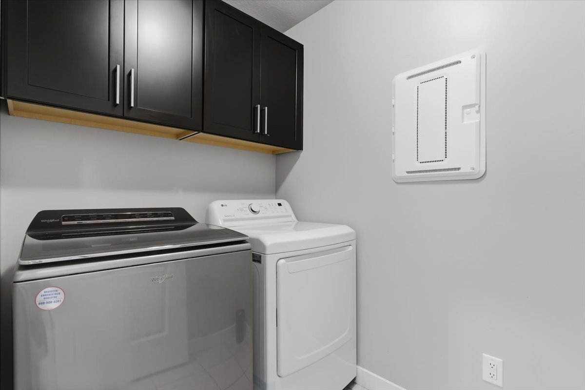 Laundry area featuring dark cabinetry, natural wood-finish trim, and light gray walls