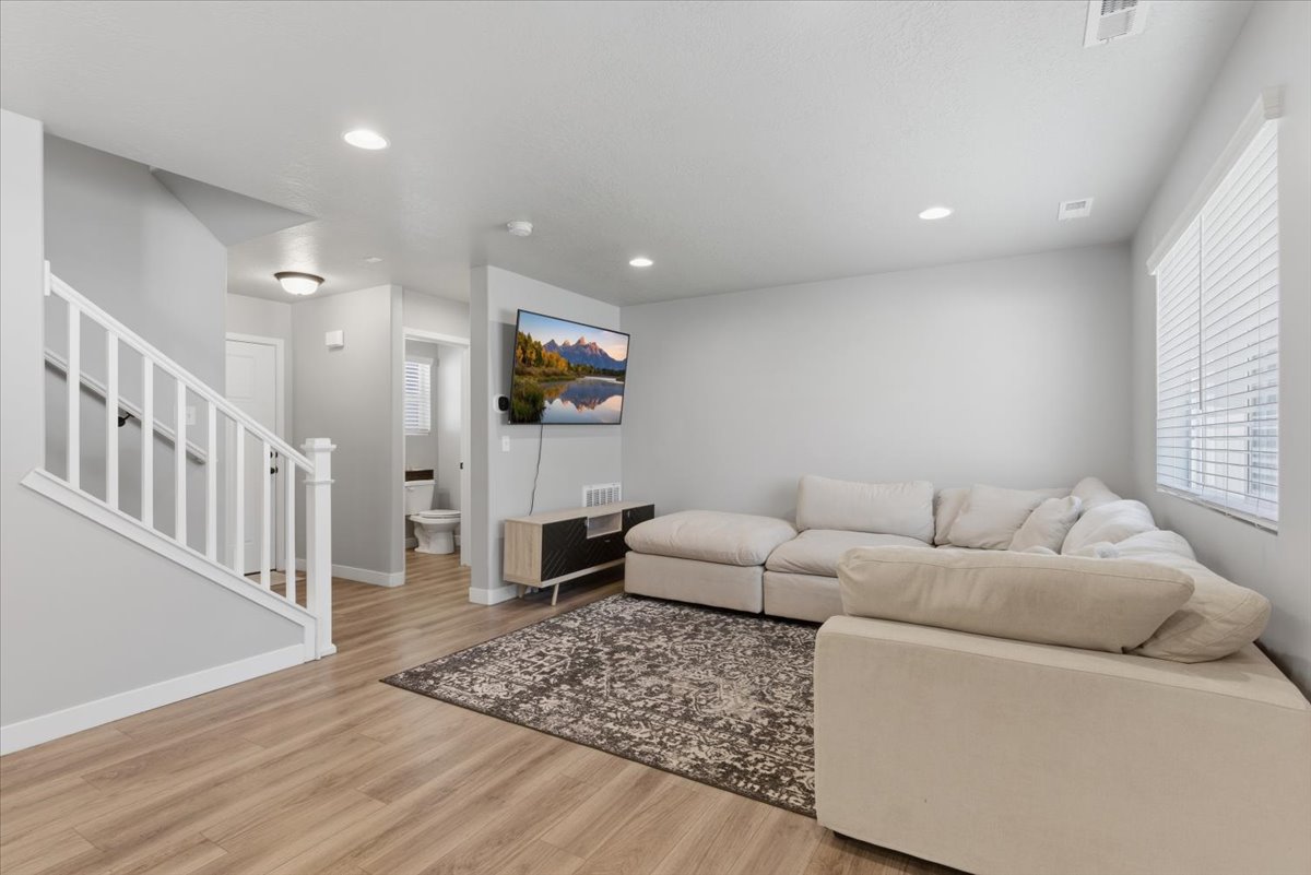 Spacious living area featuring wood-finish flooring, recessed lighting, and a white staircase with a contrasting handrail