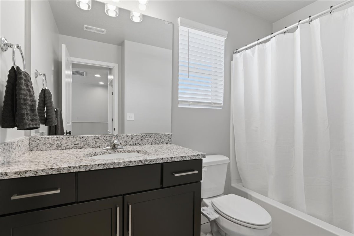 Bathroom featuring a dark wood-finish vanity with a speckled countertop, a large mirror, a white bathtub, and a window with blinds