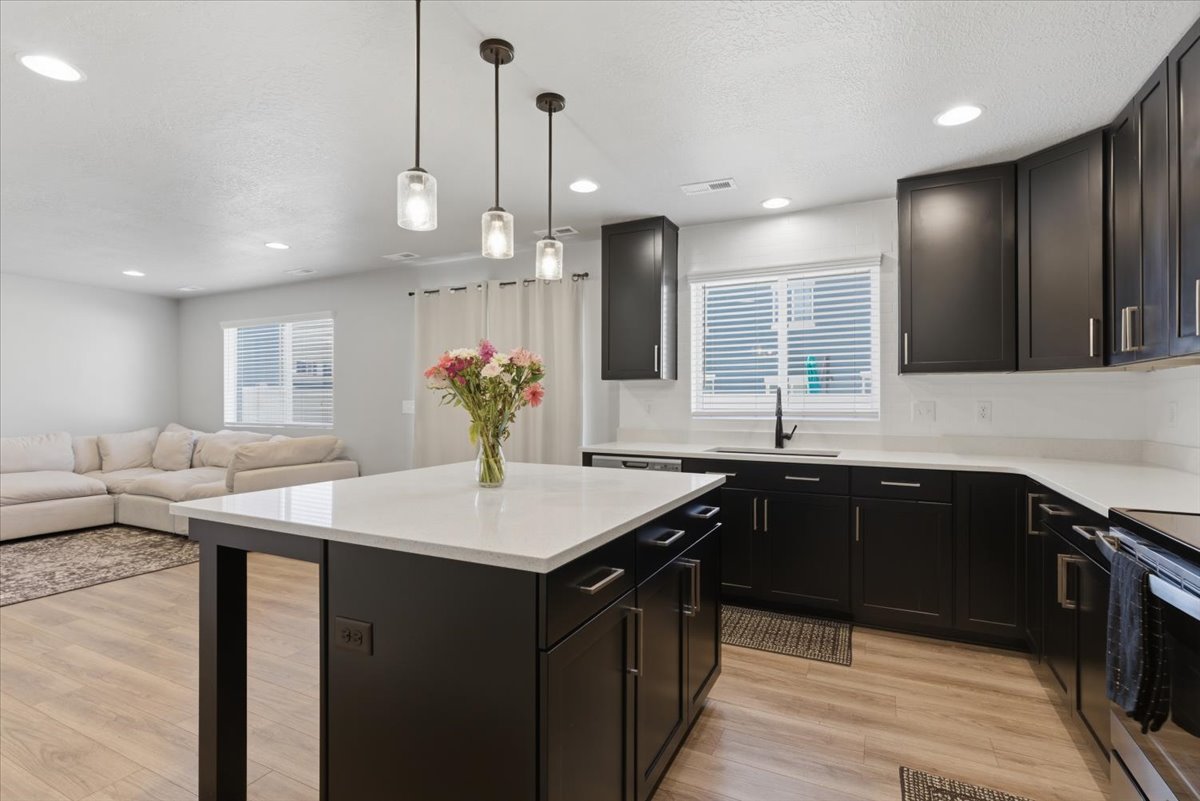 Kitchen featuring a central island with white countertop, dark cabinetry with bar pull hardware, wood-finish flooring, and recessed lighting
