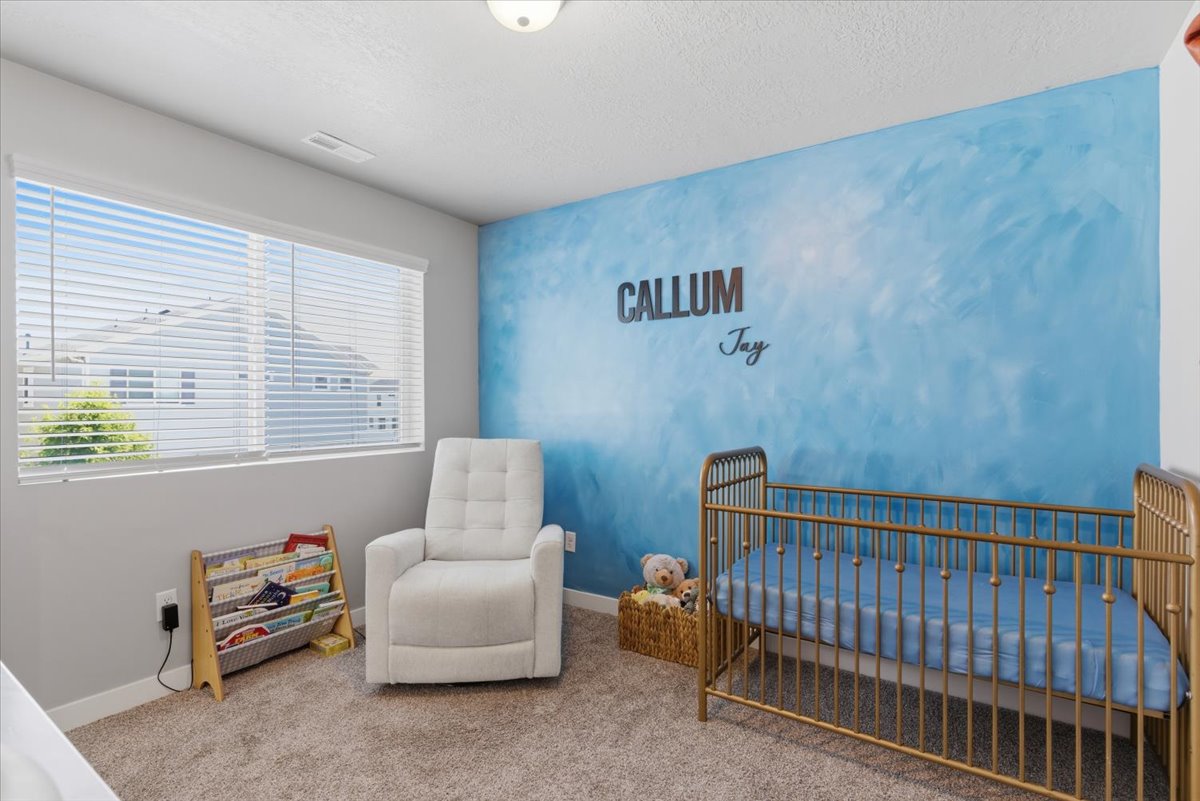 Bedroom featuring a decorative blue accent wall, neutral carpeting, and a large window with blinds