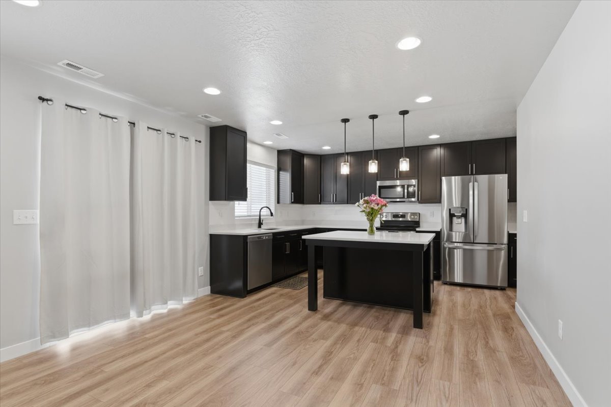 Modern kitchen featuring dark cabinetry, stainless steel appliances, and a central island with a light-toned countertop