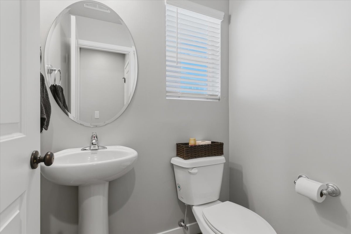 Pedestal sink with chrome faucet, circular mirror, and window with horizontal blinds