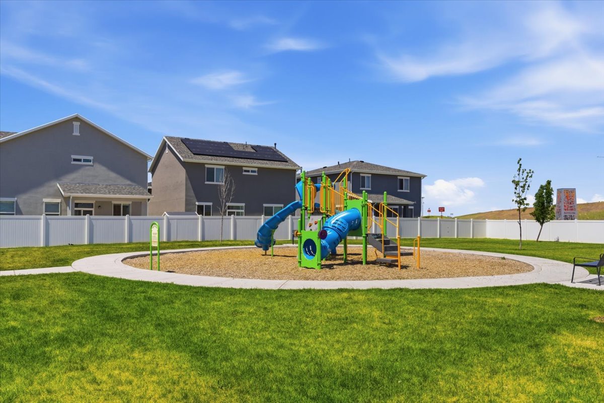 Community playground featuring a colorful playset with slides and climbing structures, surrounded by wood chip surfacing and a paved walking path