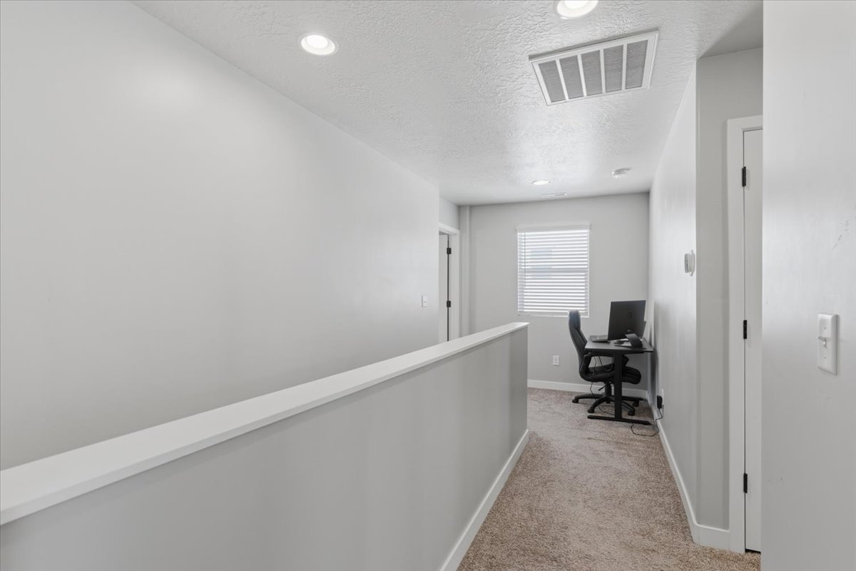 Carpeted hallway with a neutral color palette, recessed lighting, and a white railing