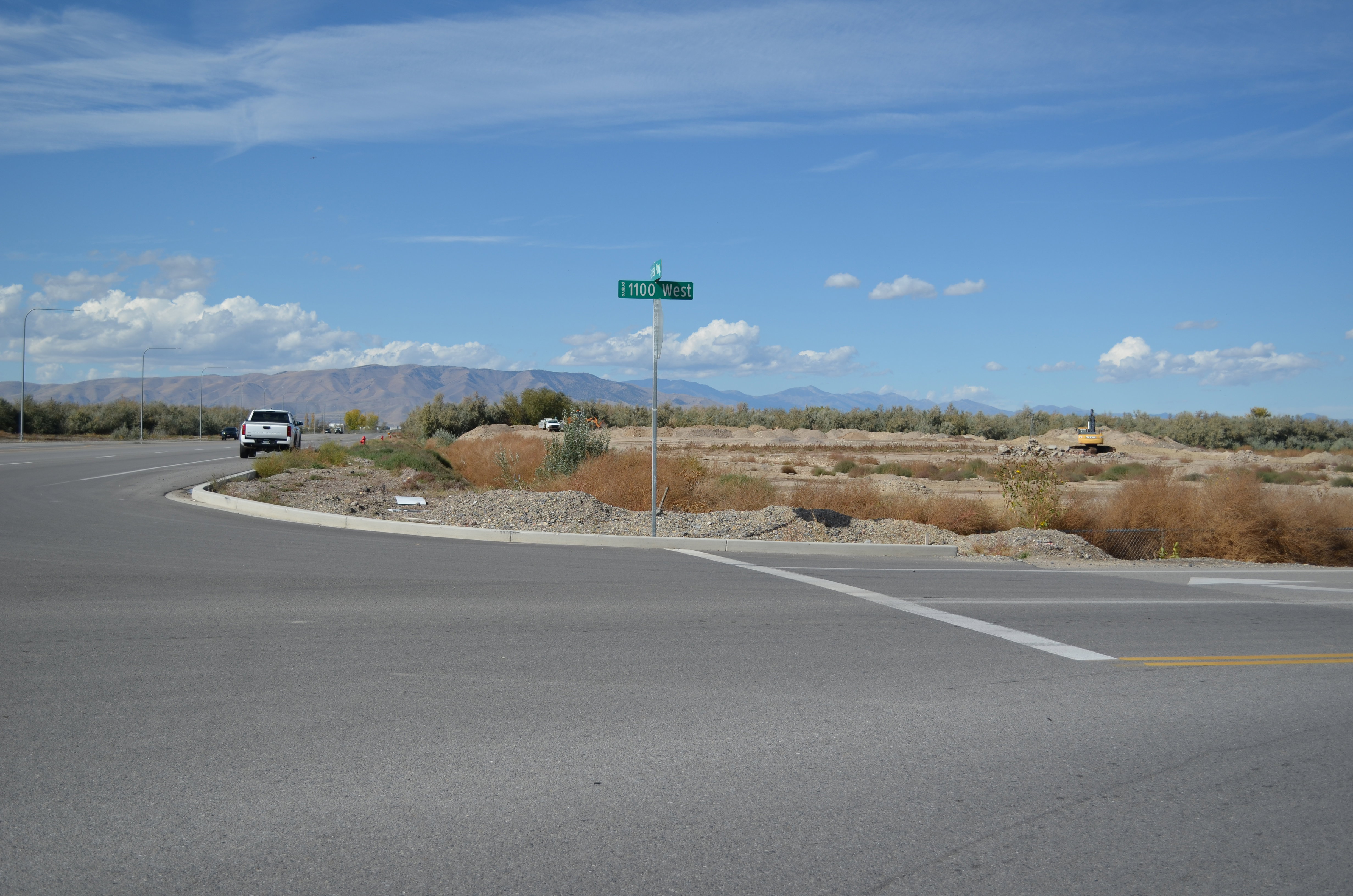 Paved road at an intersection, featuring a street sign, curb, and visible mountainous backdrop