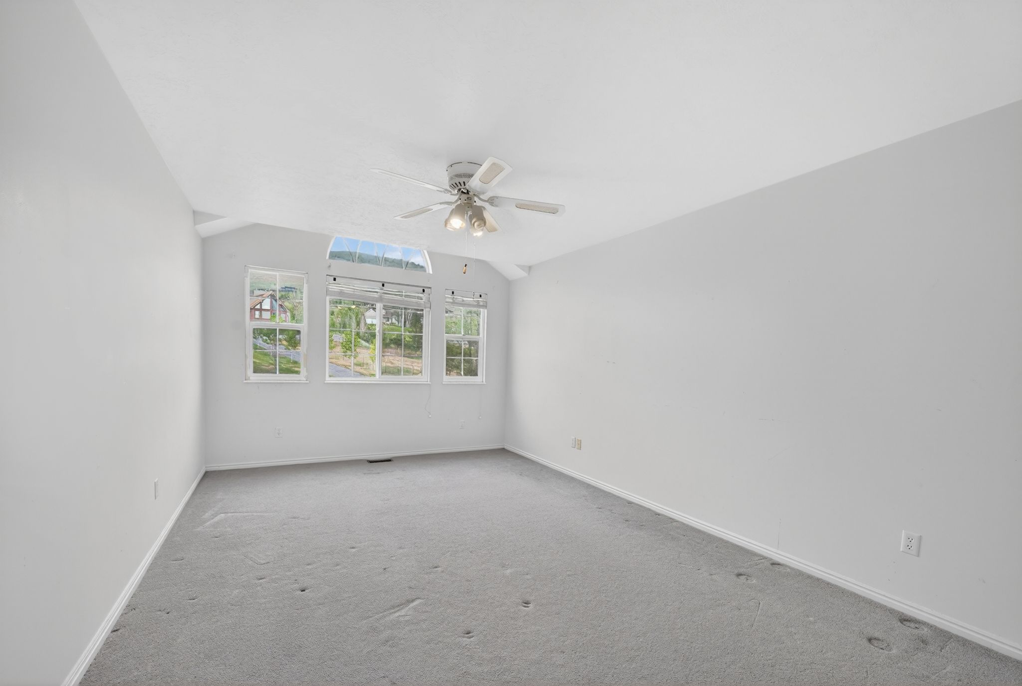 Expansive room with vaulted ceilings, light gray carpeting, and multiple windows providing ample ambient light