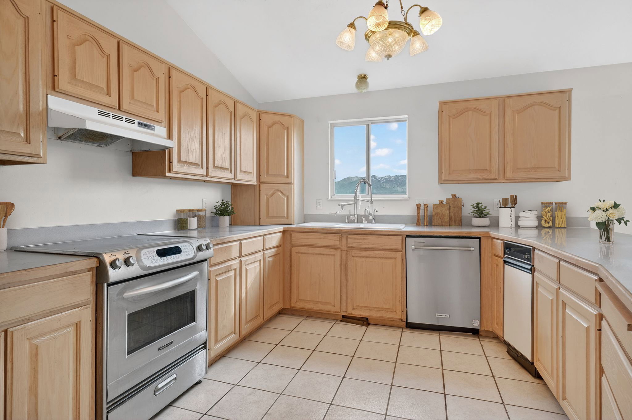 Spacious kitchen featuring extensive light wood cabinetry, a stainless steel range, a stainless steel dishwasher, a dual-basin sink, and tile flooring