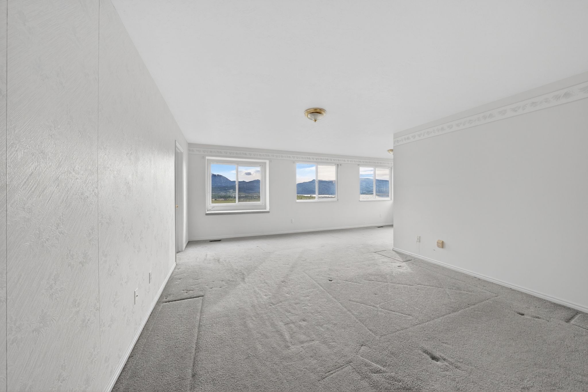 Spacious interior room with light gray carpet flooring and multiple windows framing mountain scenery
