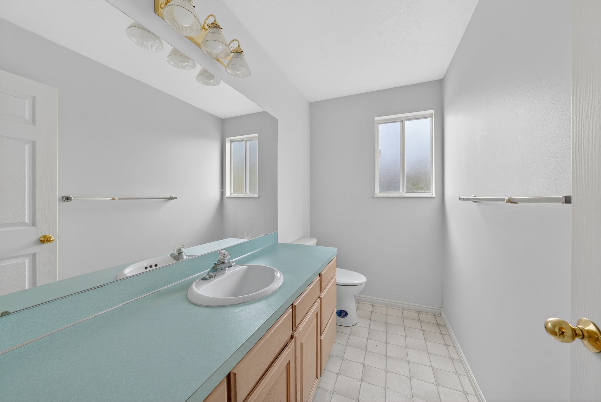 Bathroom featuring a light-colored vanity with an oval sink, a wall-mounted mirror, and a multi-bulb light fixture