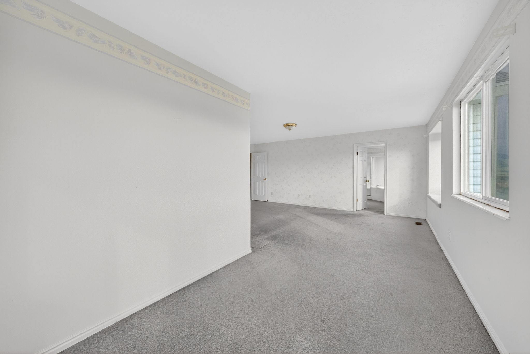 Spacious room featuring light gray carpet, white painted walls, and multiple windows