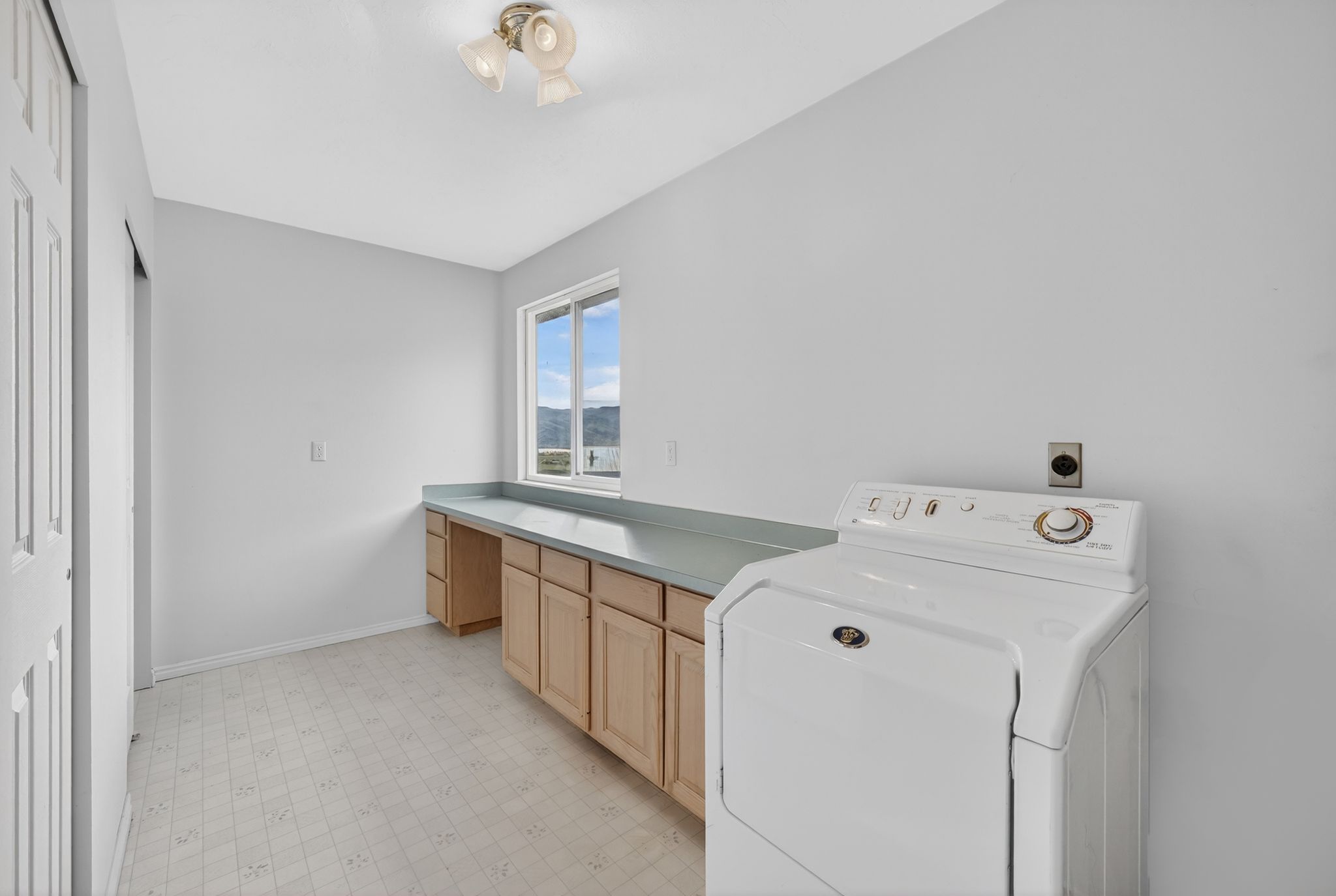 Dedicated laundry area featuring a built-in countertop, wood-finish cabinetry, patterned flooring, and a window with exterior scenery