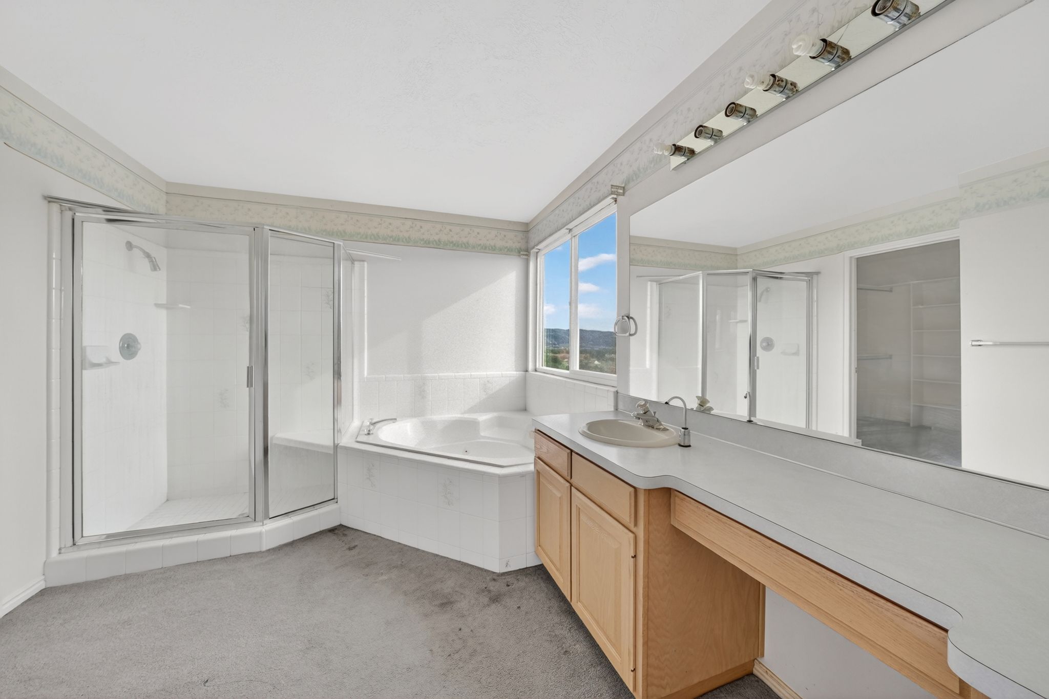 Bathroom featuring a glass-enclosed shower, corner soaking tub, and an extended vanity with dual-toned cabinetry and a single basin sink