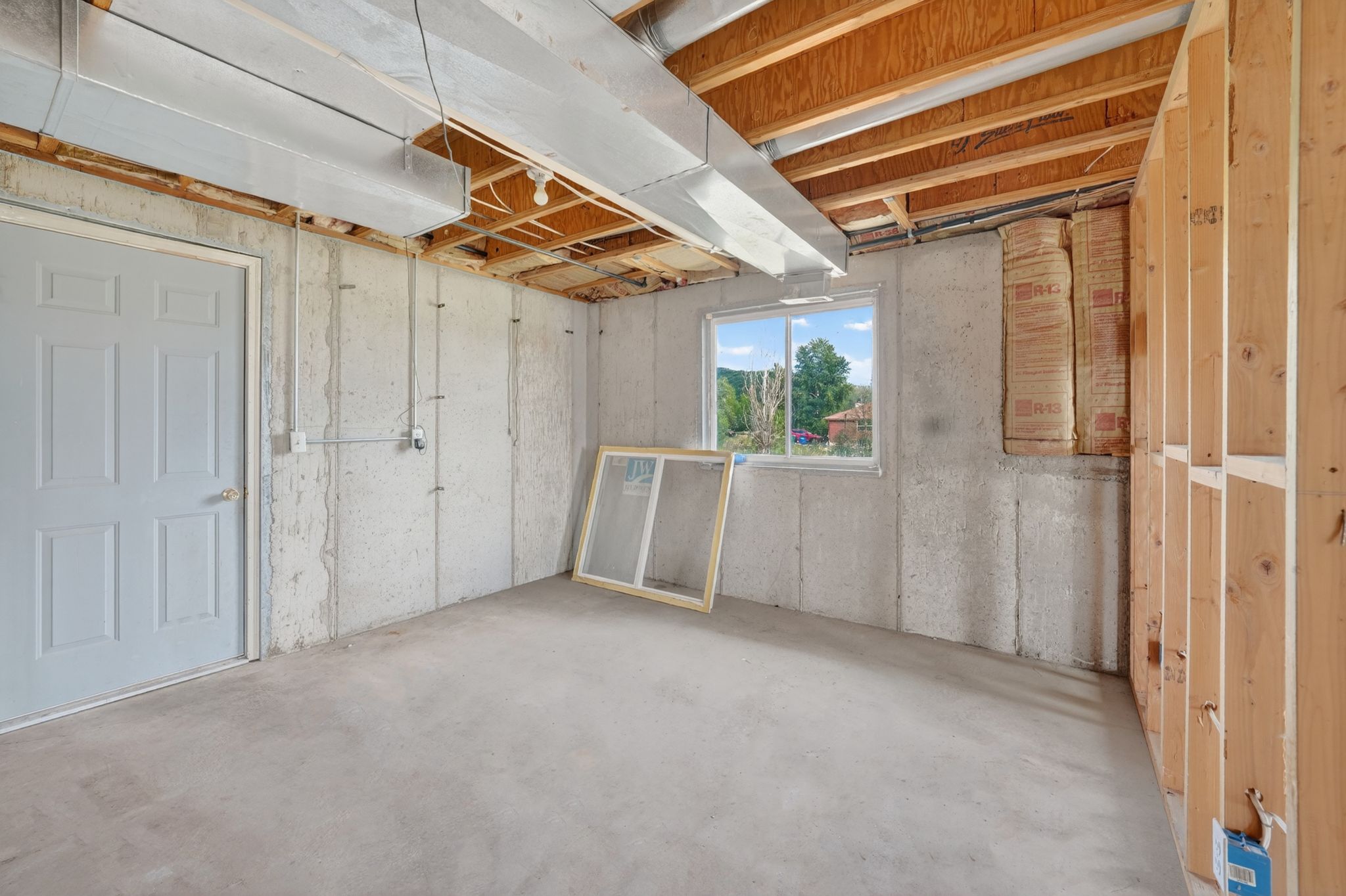Unfinished basement space featuring concrete walls and flooring, exposed ceiling joists, and a perimeter wall framed with wood studs