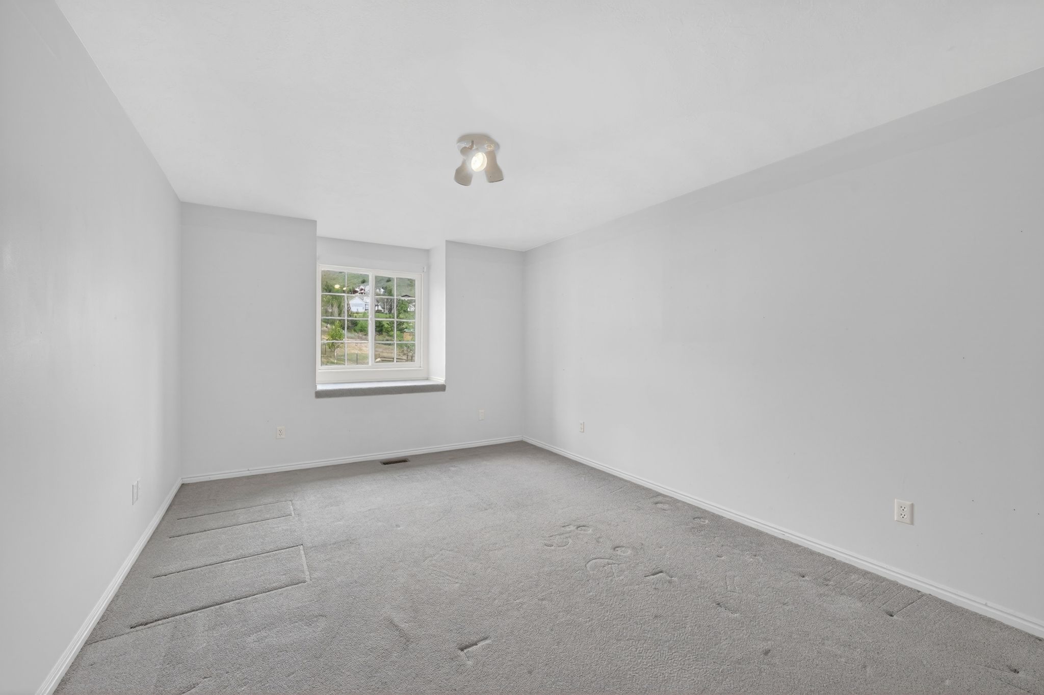 Room with light gray carpeting, neutral wall finishes, and a single window offering natural light