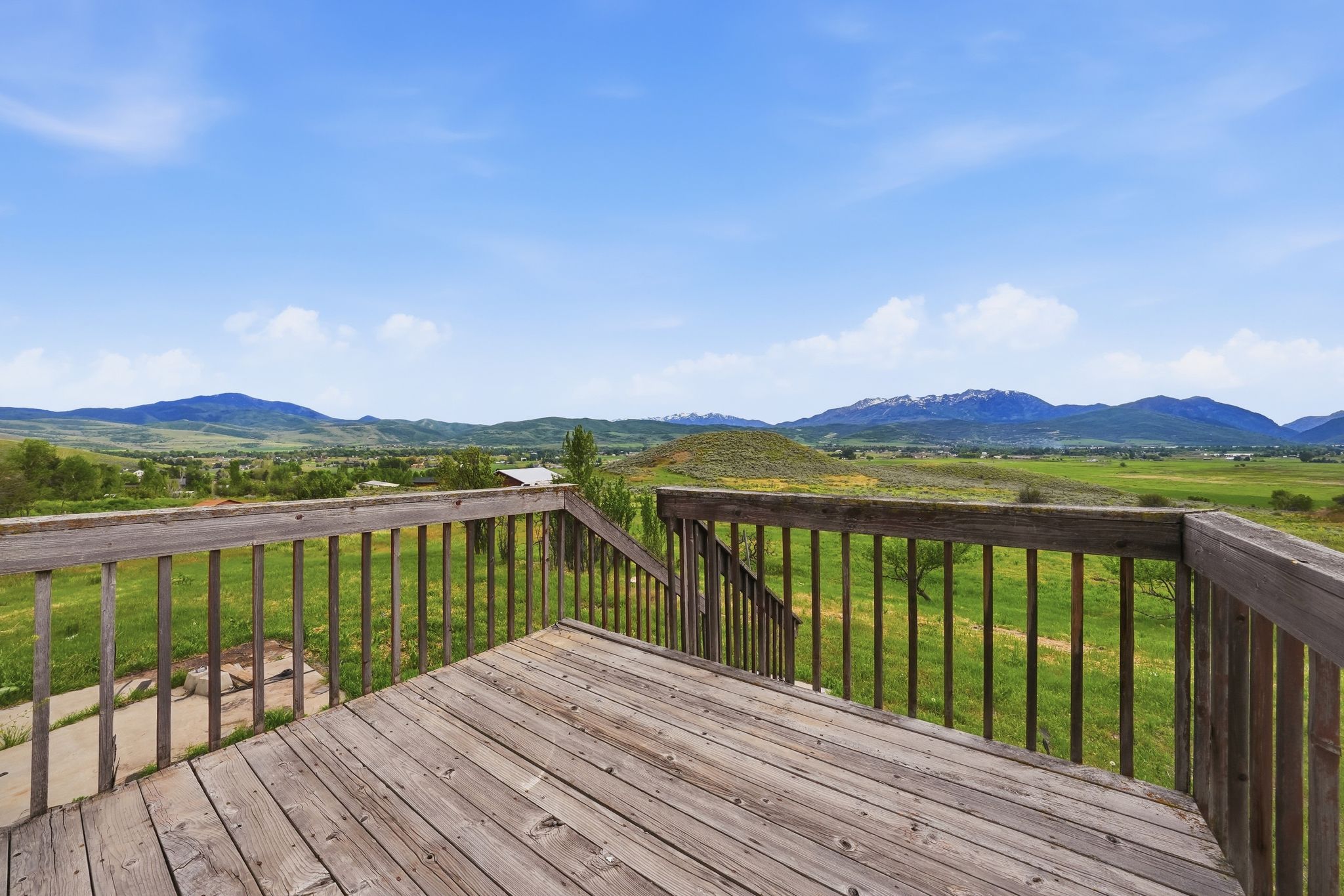 Wood deck with railing overlooking expansive green fields and distant mountains