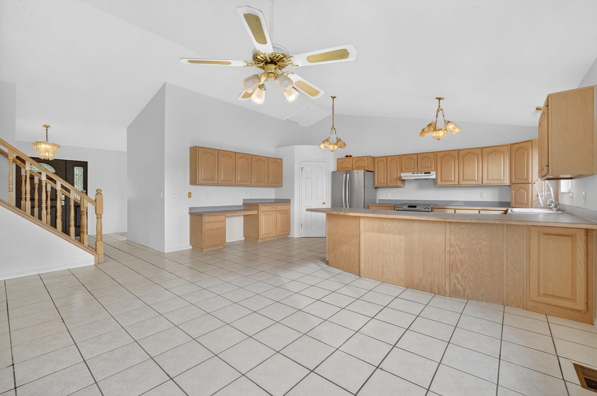 Open-concept kitchen featuring light wood cabinetry, a stainless steel refrigerator, and a built-in desk area