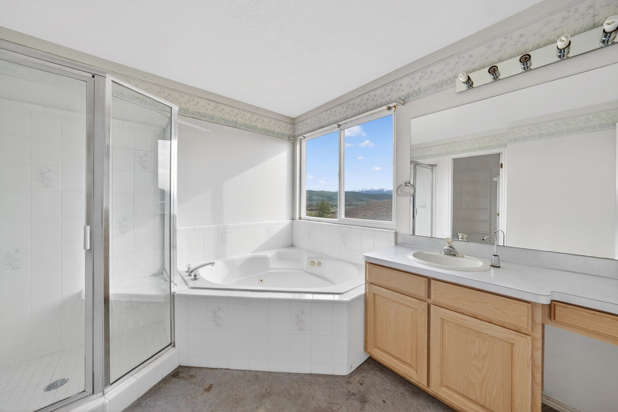 Bathroom featuring a corner jetted tub, a separate glass-enclosed shower, a double vanity with an integrated sink, wood-finish cabinetry, and a large window