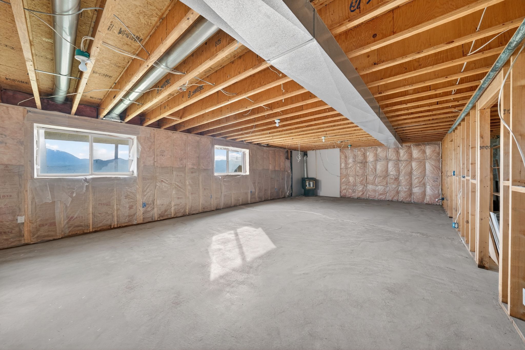 Unfinished basement space featuring exposed wood joists, structural framing, and two windows