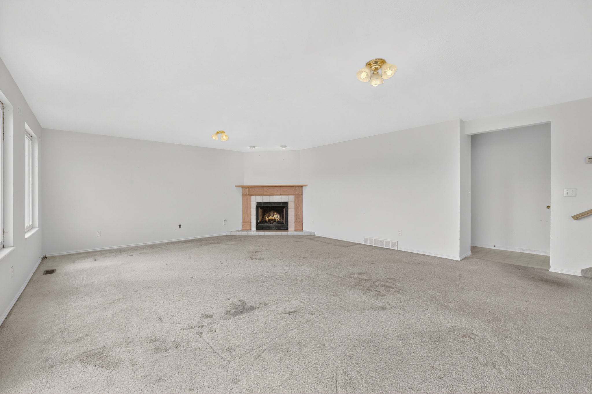 Spacious room featuring a corner fireplace with a tan tile surround and hearth, multiple windows, and two ceiling-mounted light fixtures