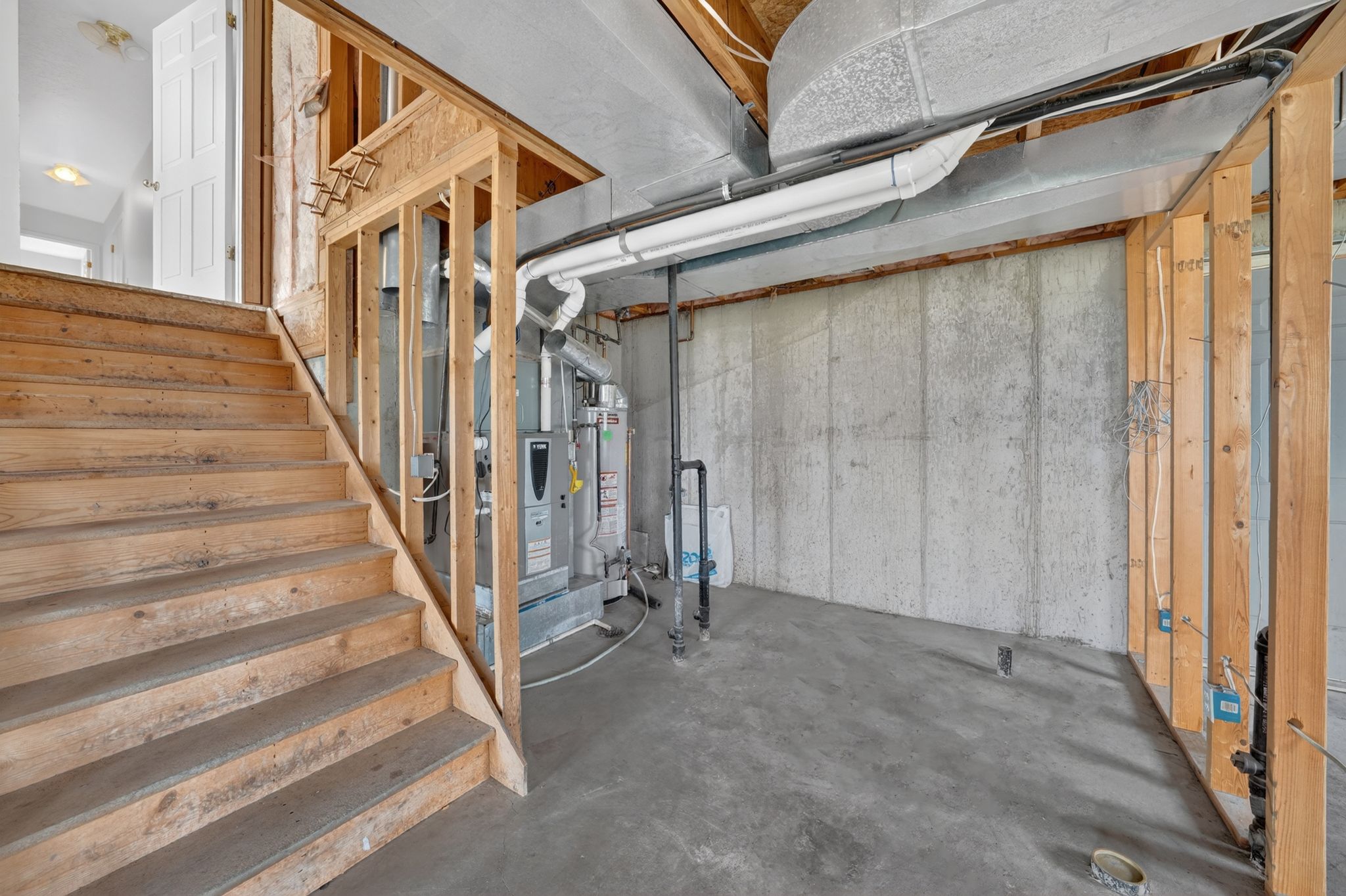 Unfinished basement space featuring a visible furnace system, concrete walls, concrete flooring, and exposed wood framing