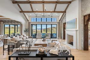 Spacious open-concept living area featuring exposed wood beams, a prominent fireplace with a herringbone pattern firebox, and light wood-finish flooring
