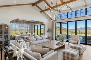 Spacious living area featuring a vaulted ceiling with exposed wood beams, a large contemporary chandelier, and wood-finish flooring