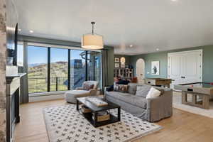 Spacious living area featuring large picture windows, wood-finish flooring, a decorative fireplace mantel, recessed lighting, and a drum pendant light fixture