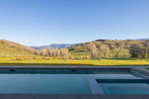 Infinity-edge pool with integrated spa and dark tile surround, set against a backdrop of rolling hills and distant snow-capped mountains