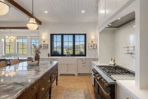 Spacious kitchen featuring a large central island with a stone countertop, a professional-grade range, full-height white cabinetry, shiplap ceiling details, and expansive windows