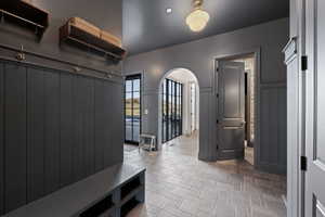 Foyer featuring wainscoting, built-in bench with shoe storage, arched doorway, and patterned tile flooring