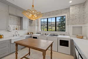 Laundry room featuring a farmhouse sink, extensive built-in cabinetry, wood-finish flooring, a contemporary overhead light fixture, and a large multi-pane window showcasing a natural landscape
