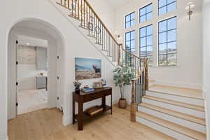 Double-height entry foyer featuring natural wood-finish flooring, a grand staircase with wood newel posts and black iron balusters, and a bank of transom windows