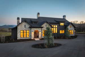 Stone and dark siding exterior featuring multiple dormer windows, a prominent arched entry, a circular drive, and a mountain backdrop